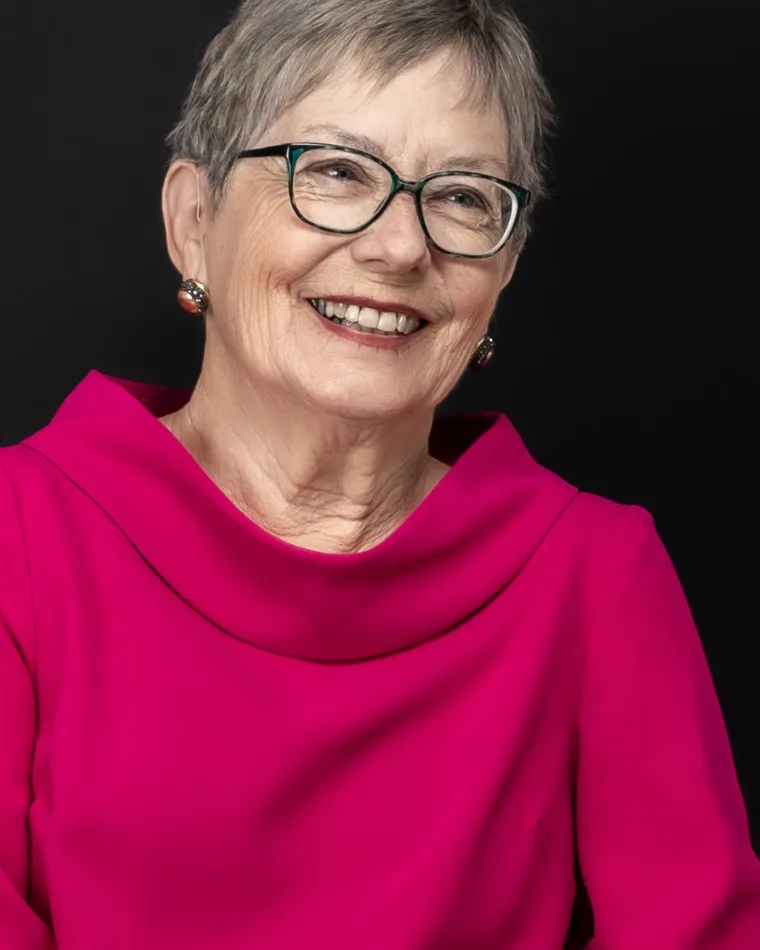 Signora sorridente con occhiali e blusa fucsia su fondo nero, ritratto di Ilia Da Lozzo